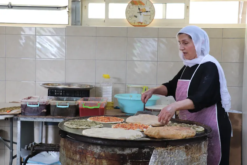 אישה בכיסוי ראש לבן מכינה מאפים על תנור עגול גדול במאפייה מקומית